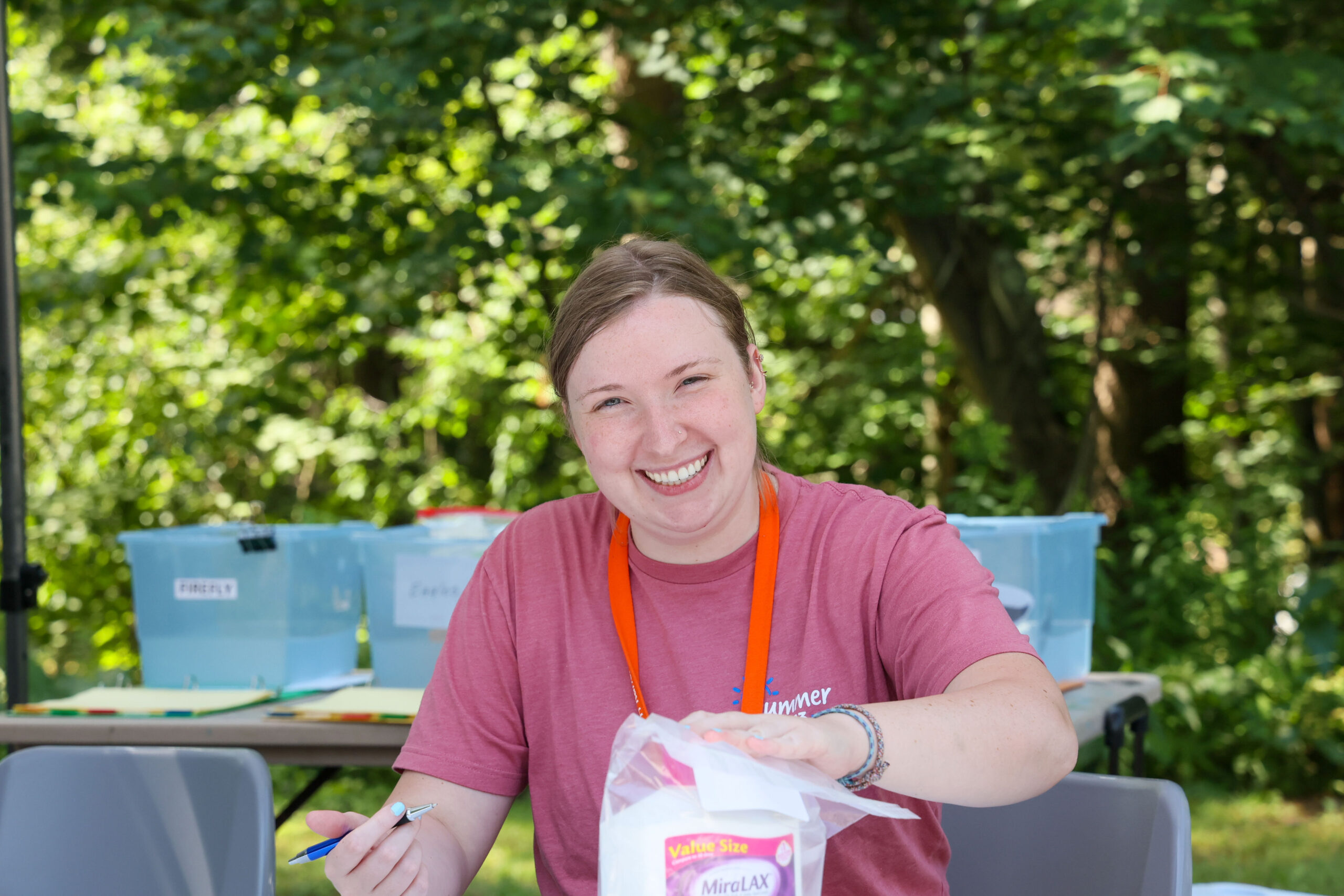 Woman in pink shirt sitting at table and smiling at camera.